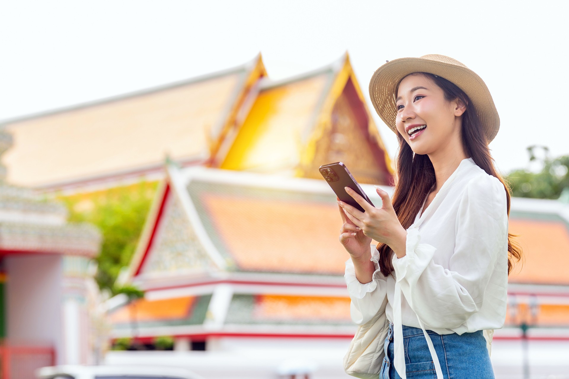 Asian female tourist using phone in front of Wat Phra Kaew and the Grand Palace, Bangkok, Thailand
