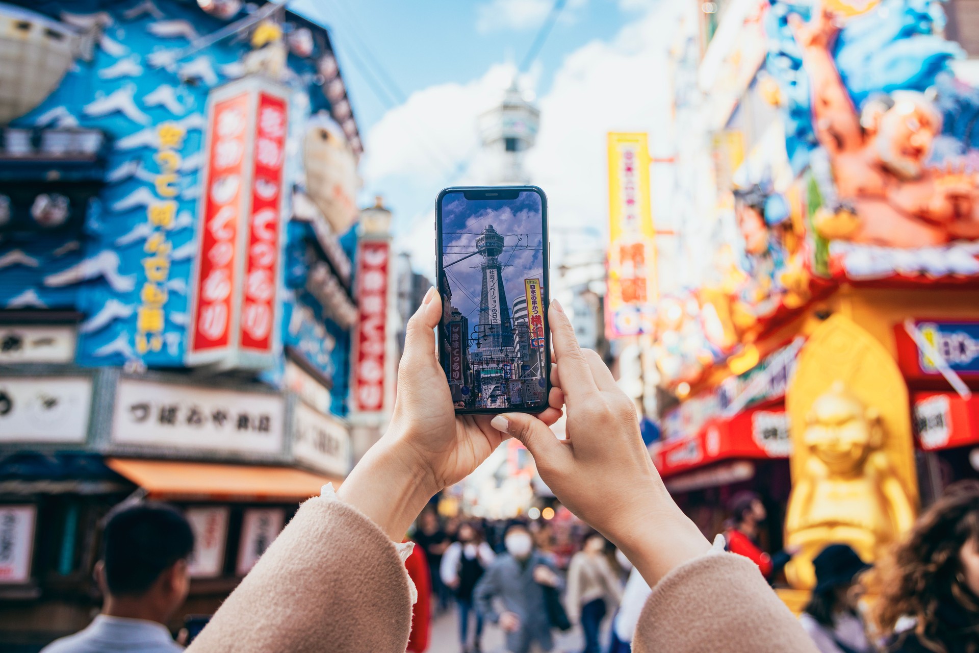 An Asian woman is sightseeing at Tsutenkaku in Osaka, Japan. She uses her smartphone to capture photos of Tsutenkaku and the surrounding scenery.